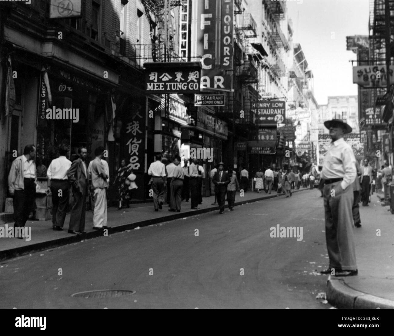 Dieses Vintage-Straßenfoto von Angelo Rizzuto, wahrscheinlich aus den 1940er Jahren, fängt an einem Sonntag eine geschäftige Szene in der Pell Street in New Yorks Chinatown ein. Fußgänger, die in zeitgenössischer Mode gekleidet sind, gehen vorbei an Geschäften mit chinesischen Schriftzeichen und englischen Schildern wie „Mee Tung Co“, „Wing Wo Chong Co“ und „Henry Low Restaurant“. Stockfoto