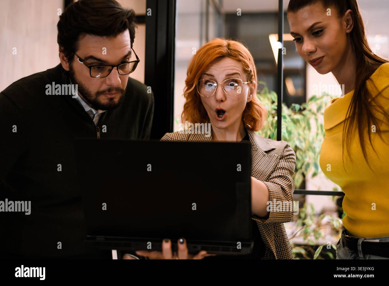 Drei Kollegen treffen sich in einem modernen Büro um einen Laptop und äußern während einer Präsentation oder Daten auf dem Bildschirm Überraschung und Begeisterung Stockfoto