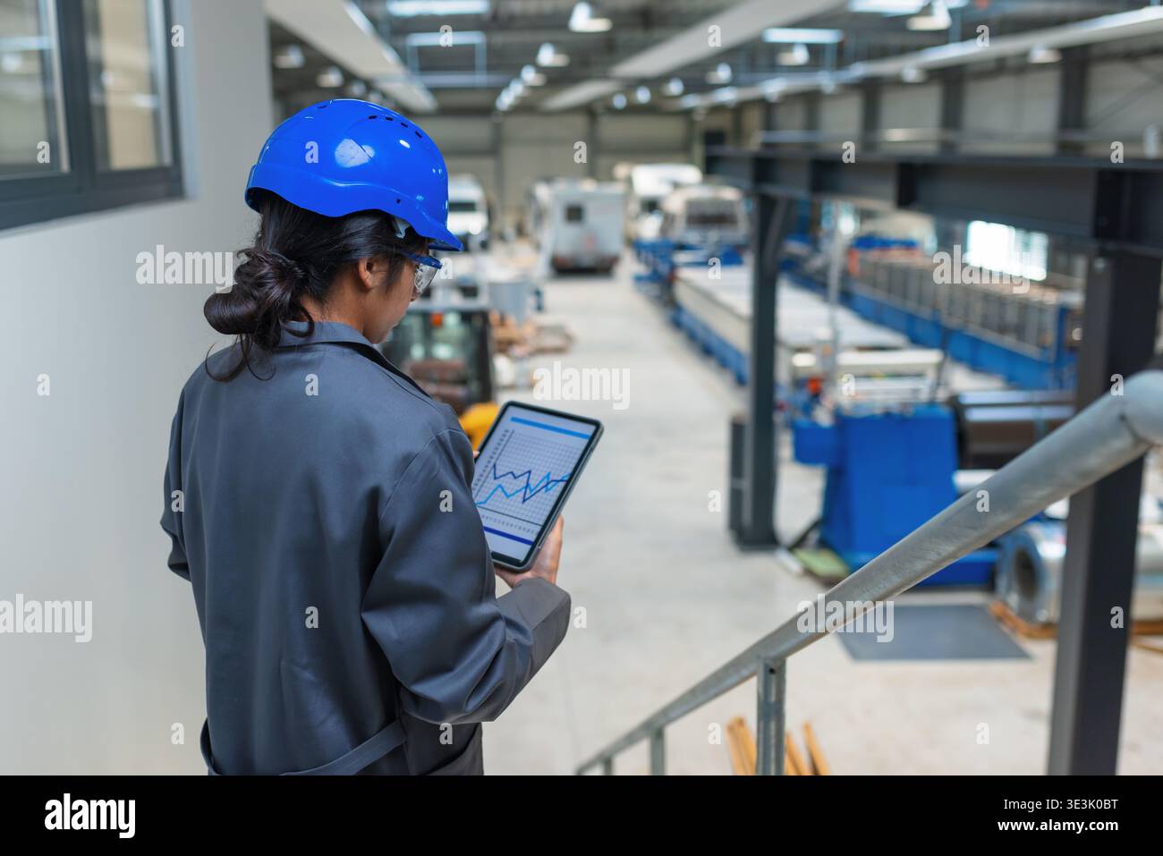 Eine indische Ingenieurin steht in einer Fabrik und hält ein Tablet. Sie überwacht Maschinen und Abläufe in einem Produktionsbereich. Stockfoto