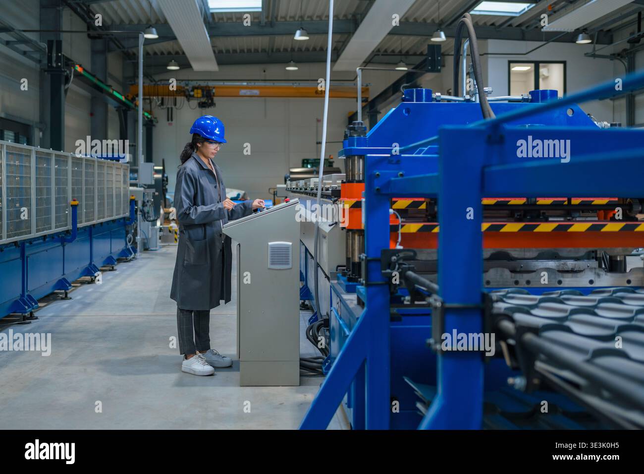 Eine indische Ingenieurin arbeitet an Maschinen in einer Fabrik, während sie Sicherheitsausrüstung trägt. Sie konzentriert sich auf ihre Aufgabe an einer Produktionslinie. Stockfoto