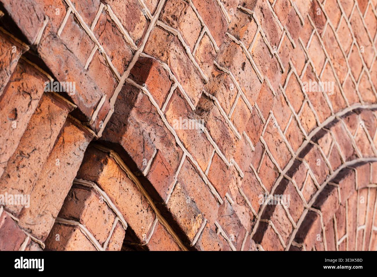 Nahaufnahme einer verwitterten roten Ziegelwand mit sich wiederholenden Bogenmustern, strukturierten Mörtelfugen und rustikalen Oberflächendetails, ideal für architektonische Zwecke Stockfoto