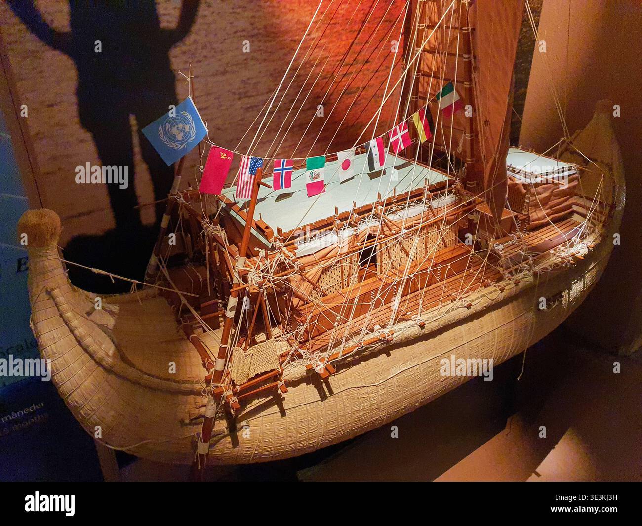Ein detailliertes Modell des Schilfbootes Ra II in einem Museum mit dramatischer bernsteinfarbener Beleuchtung. Das Schiff hat einen gebogenen Rumpf Stockfoto