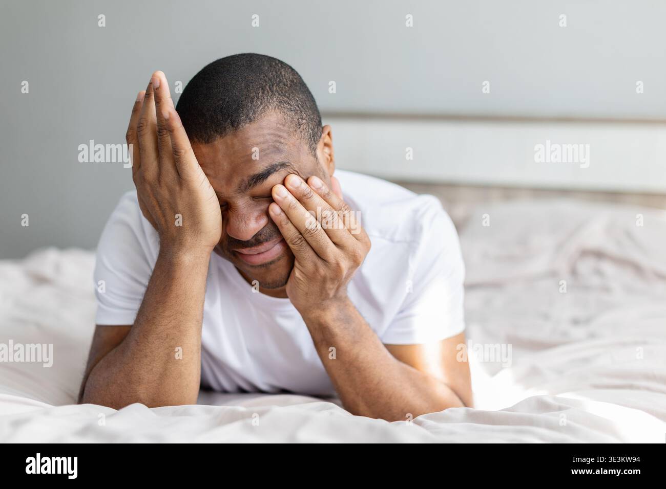 Junger afroamerikanischer Mann, der sich die Augen reibt, während er auf dem Bett liegt Stockfoto