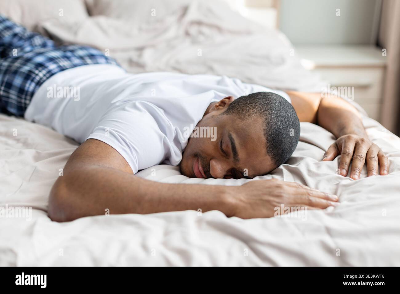 Junger schwarzer Mann, der friedlich auf dem Bett schläft, im Morgenlicht, und sich bequem ausruht Stockfoto