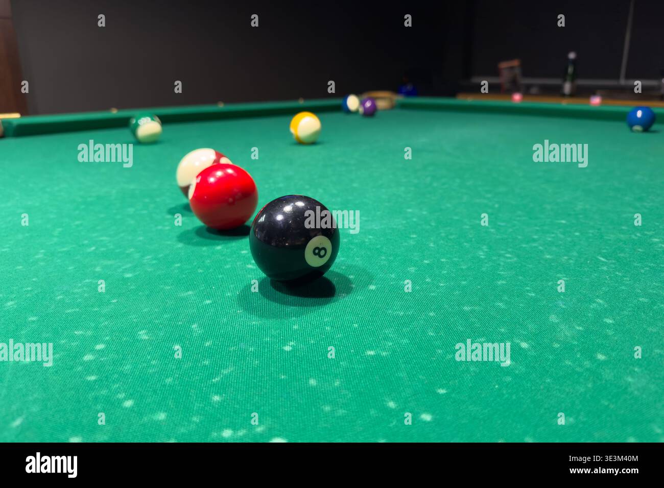 Die Bälle sind auf einem grünen Filzbillardtisch unter fokussierter Beleuchtung angeordnet. Die Spieler denken über ihre nächsten Züge in einem Spiel nach, das Geschick und Stretch erfordert Stockfoto