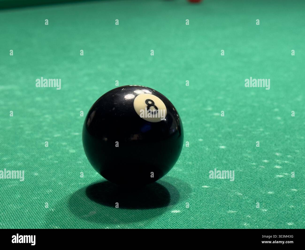Eine Nahaufnahme eines Billardtisches mit einer einsamen schwarzen Acht-Kugel auf leuchtendem grünem Filz, die das Ballarrangement und die Strukturen in einem spielorientierten Atmo zeigt Stockfoto
