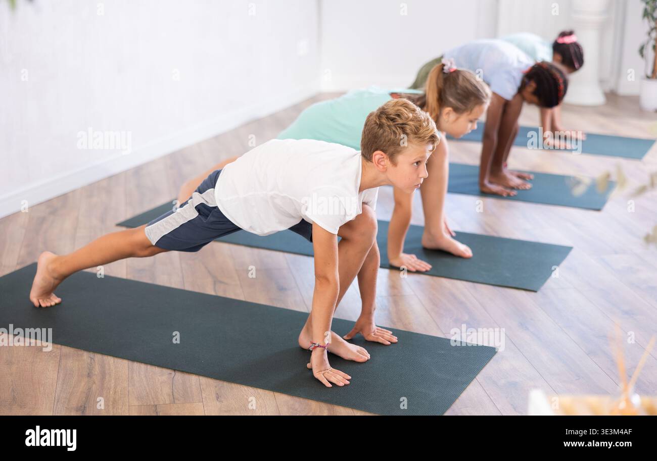 Multiethnische Jugendkinder in Hundestellung beim Yoga-Unterricht im Studio Stockfoto