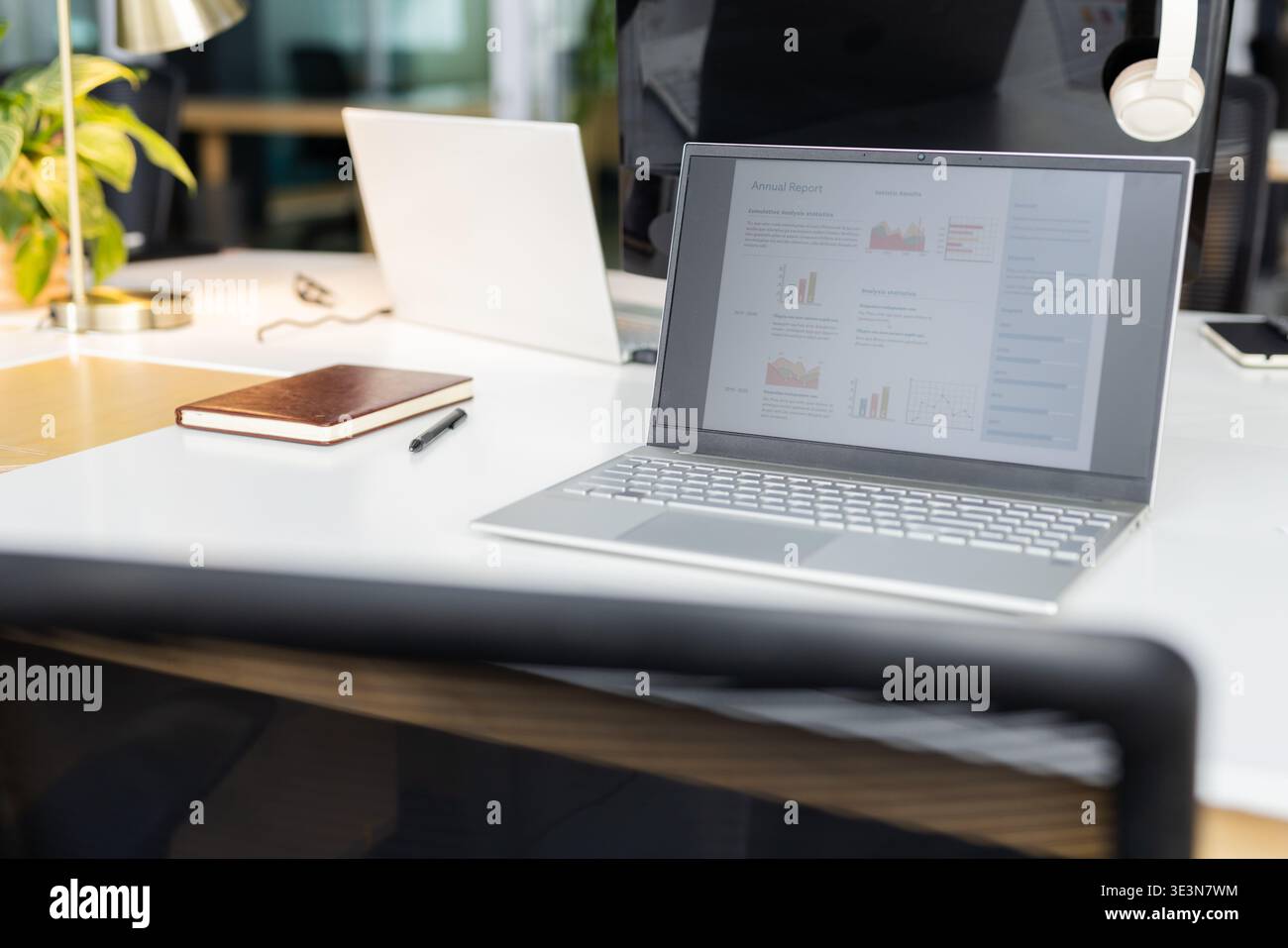Silver Laptop zeigt den Jahresbericht auf dem Schreibtisch mit Notebook, Stift, Pflanze, Kopfhörern und Lampe Stockfoto