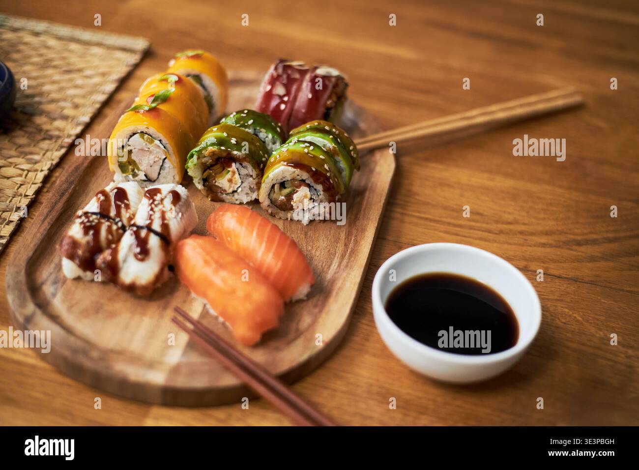 Traditionelle asiatische Küche mit verschiedenen Sushi-Brötchen und Nigiri auf Holzplatte mit Essstäbchen und Sojasauce, die kulturelle kulinarische Präsentation und Vielfalt hervorhebt Stockfoto