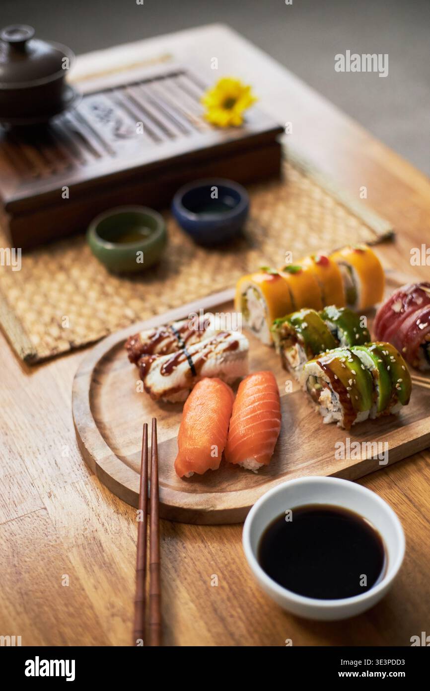 Verschiedene Sushi-Brötchen und Nigiri auf Holzbrett mit Sojasauce und Essstäbchen auf dem Tisch, traditionelle asiatische Küche für ein kulturelles kulinarisches Erlebnis Stockfoto