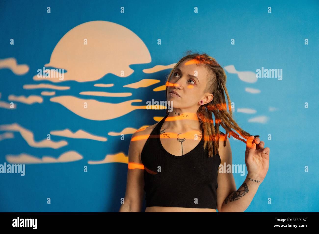 Frau mit Dreadlocks und Tattoos, die sich unter projiziertem Licht und Mondwandkunst posiert Stockfoto