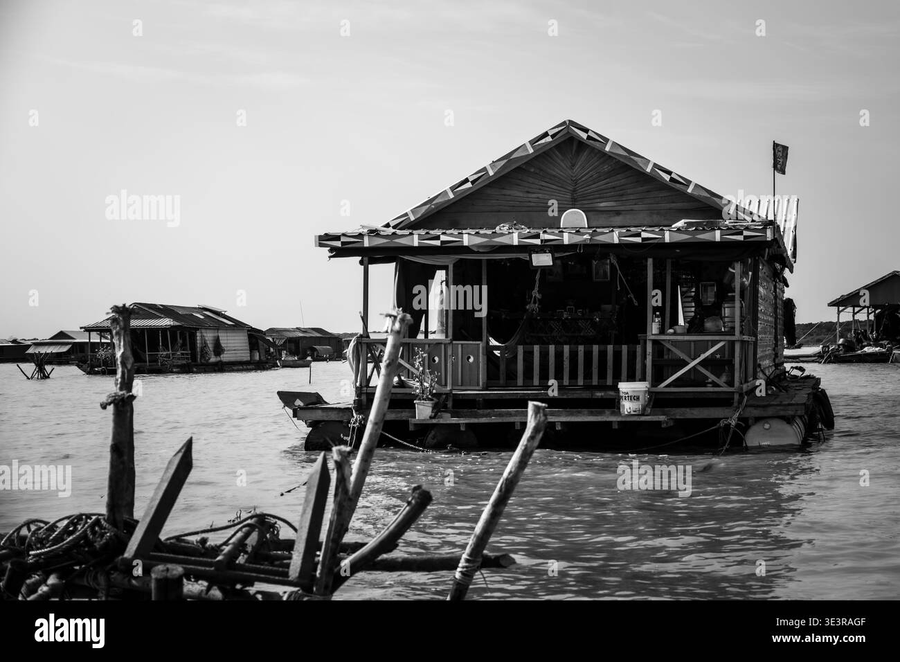 Hölzernes schwimmendes Haus mit dekoriertem Dach auf dem Tonle SAP See mit anderen Wohnungen des schwimmenden Dorfes sichtbar dahinter, Siem Reap, Kambodscha. Stockfoto