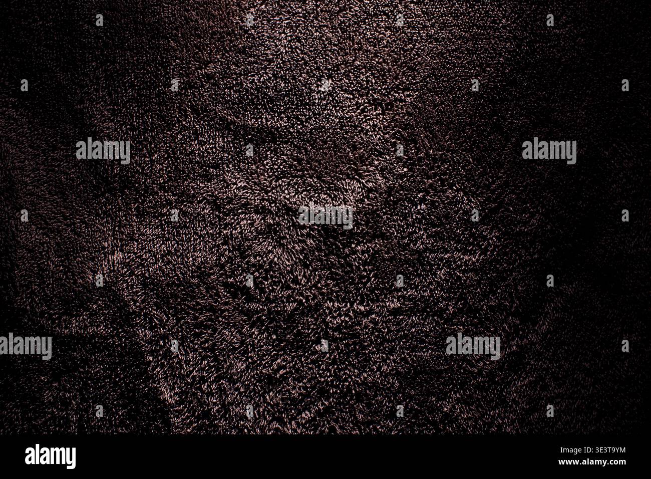 Makroaufnahme aus tiefbraunem Plüschfrottee mit detaillierten Stapelschlaufen und dramatischer Beleuchtung mit stimmungsvollen Schatten für einen eleganten Hintergrund. Stockfoto
