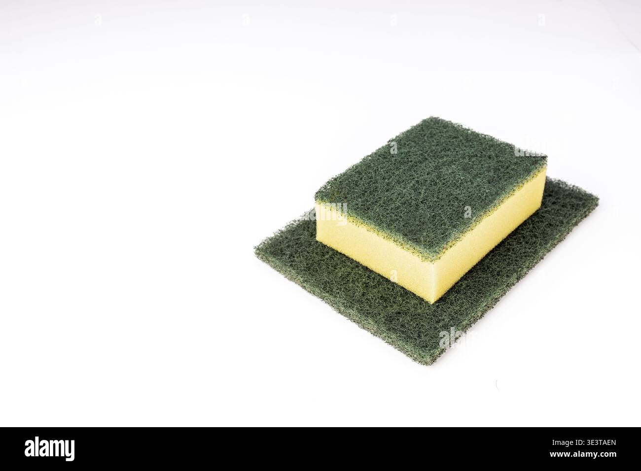 Ein brandneuer, zweilagiger Küchenschwamm mit gelbem Schaumboden und grüner Scheuerfläche sitzt auf einem größeren, flachen grünen Scheuerschwamm, bo Stockfoto