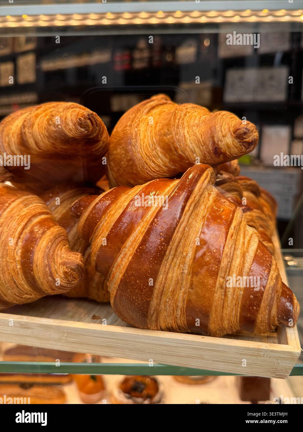 Nahaufnahme von Buttercroissants auf einer Pariser Backstube mit goldenen Schichten, schuppiger Textur und warmen Tönen unter natürlichem Licht - Smartphone-aufgenommenes Stockfoto