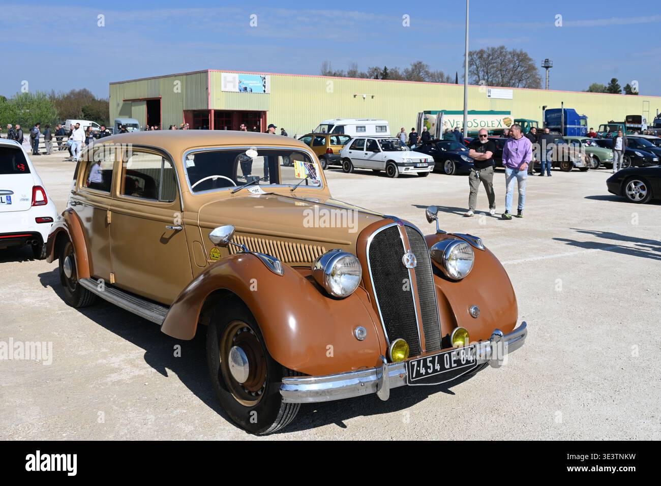 Ein paar männliche Freunde spazieren an einem Brown Vintage Hotchkiss 686 Auto oder Automobil vorbei, das zwischen 1936 und 1952 in Frankreich hergestellt wurde. Stockfoto