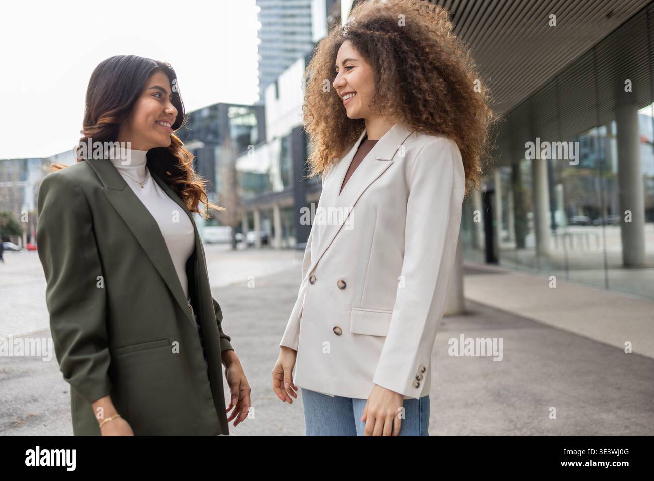 Zwei professionelle Frauen führen in einem urbanen Ambiente ein freundliches Gespräch im Freien. Beide tragen Geschäftskleidung und spiegeln Zusammenarbeit wider Stockfoto