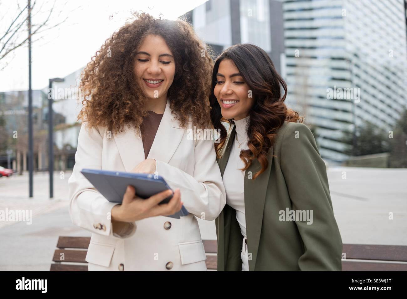 Zwei professionelle Frauen in Geschäftskleidung arbeiten mit einem digitalen Tablet im Freien zusammen und demonstrieren Teamarbeit und Freundschaft in einem urbanen Umfeld Stockfoto