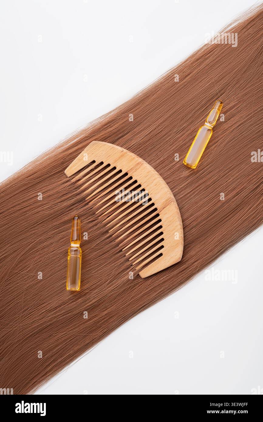 Ein Holzkamm liegt neben zwei Fläschchen Haarserum auf seidenbraunem Haar auf. Dieses Bild fängt die Essenz der natürlichen Haarpflege und starke, gesunde h Stockfoto