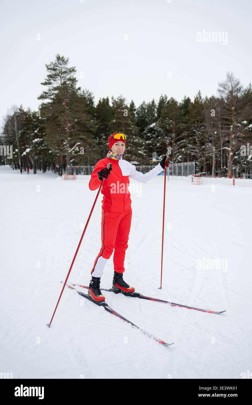 Ein Skilanglauf, der einen verschneiten Tag vor einer Waldkulisse genießt. In rot-weiß gekleidet, navigieren sie durch das verschneite Gelände mit Geschick unter einem Stockfoto