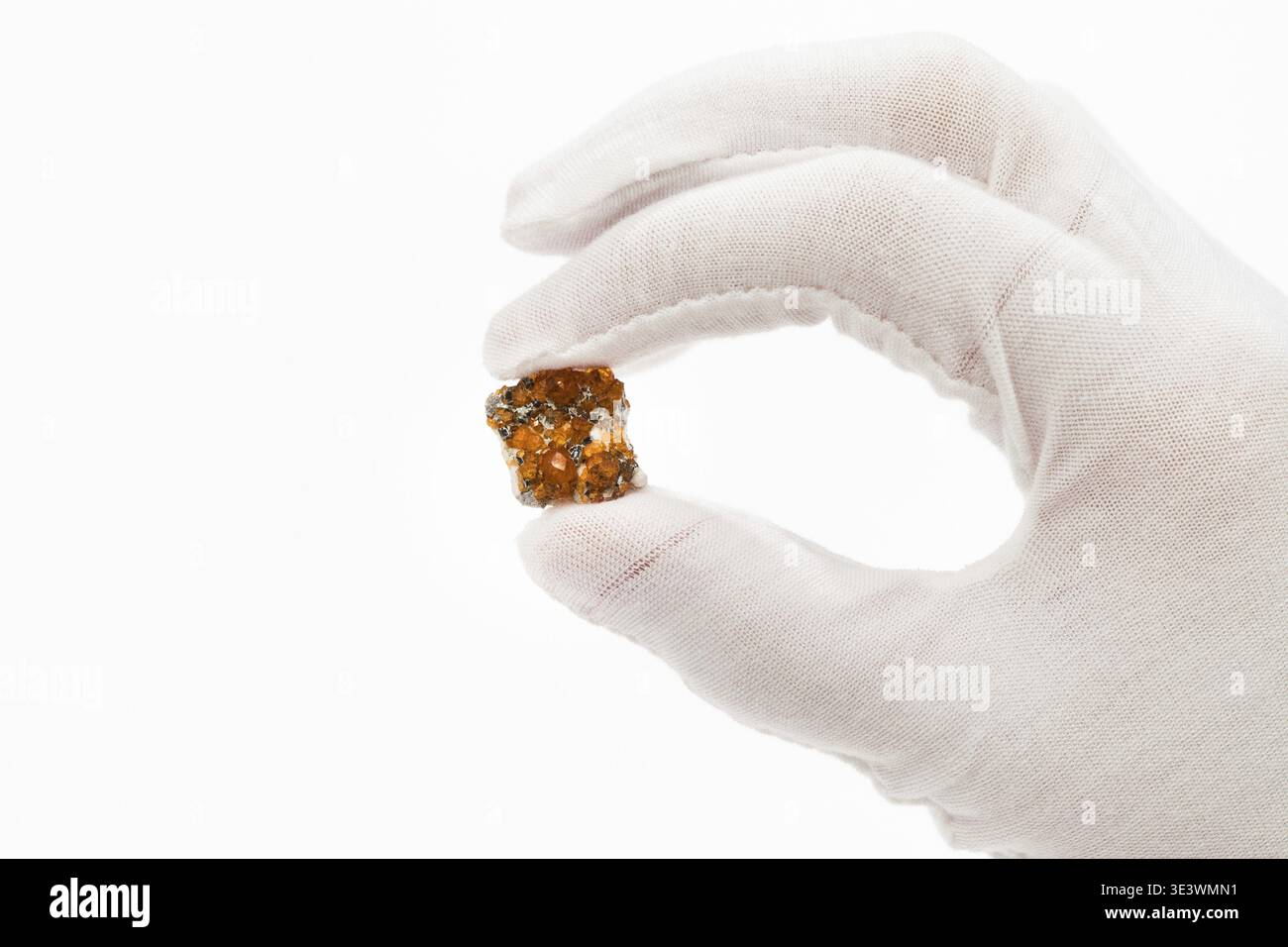Finger in weißen Handschuhen, die Spessartitkristalle auf weißem Hintergrund halten Stockfoto