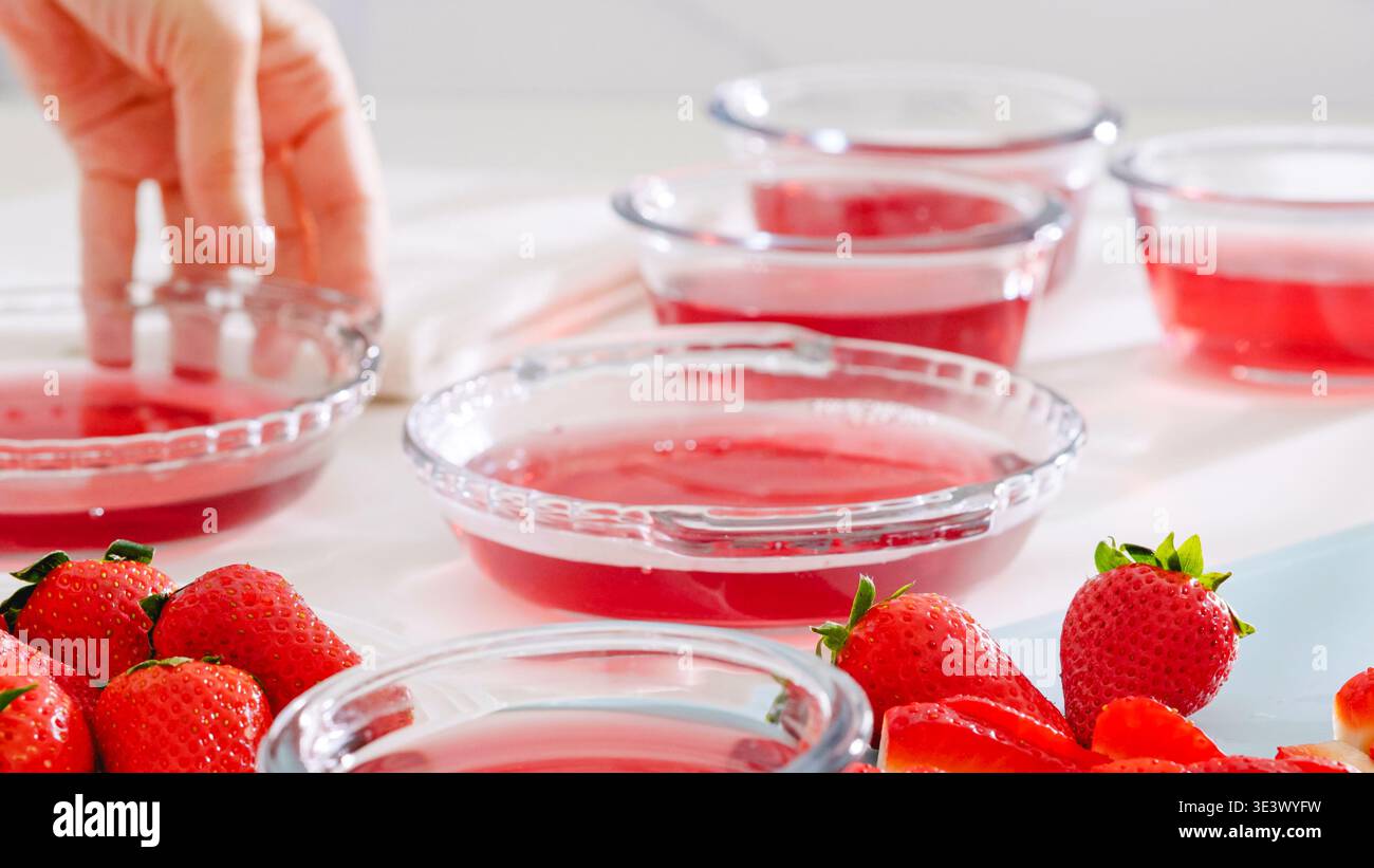 Geben Sie von Hand eine Glasschale mit Erdbeergelee unter andere Portionen. Stockfoto