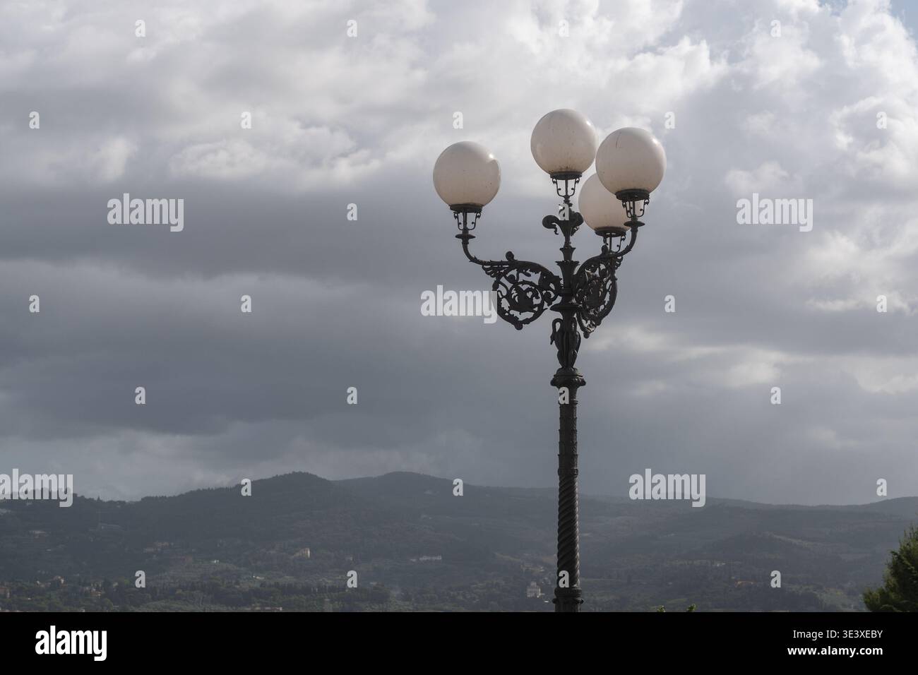 Klassische Straßenlaterne, die sich vor bewölktem Himmel und weit entfernten Bergen abhebt. Moody Atmosphäre, Reisen und minimales Landschaftskonzept Stockfoto