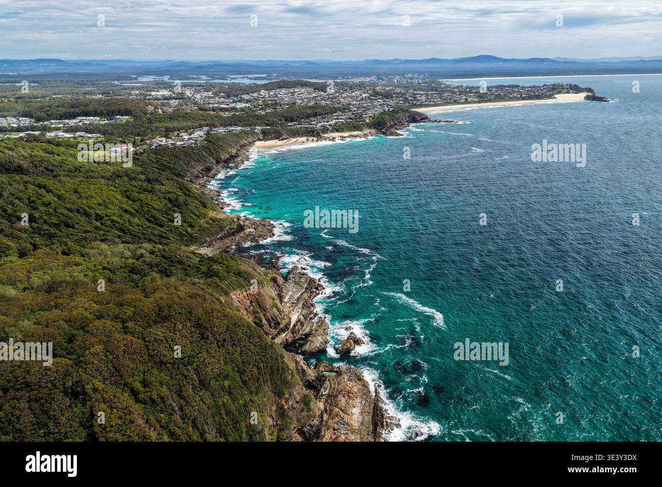 Drohnenblick auf eine felsige Küste, die in Richtung Burgess Beach und One Mile Beach in Forster führt. Die Perspektive fängt zerklüftete Küstenformationen ein Stockfoto