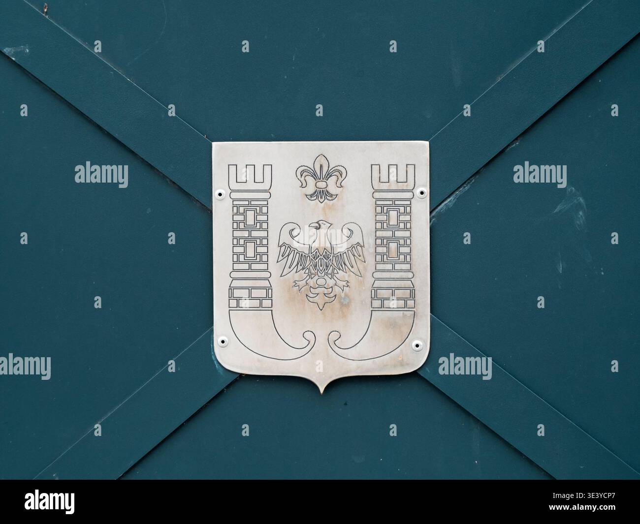 Silbernes Emblem an dunkelgrüner Metalltür. Das Emblem zeigt Adler, Krone und dekorative Borten. Klassischer heraldischer Stil, leicht verwitterte Oberfläche. Symboli Stockfoto