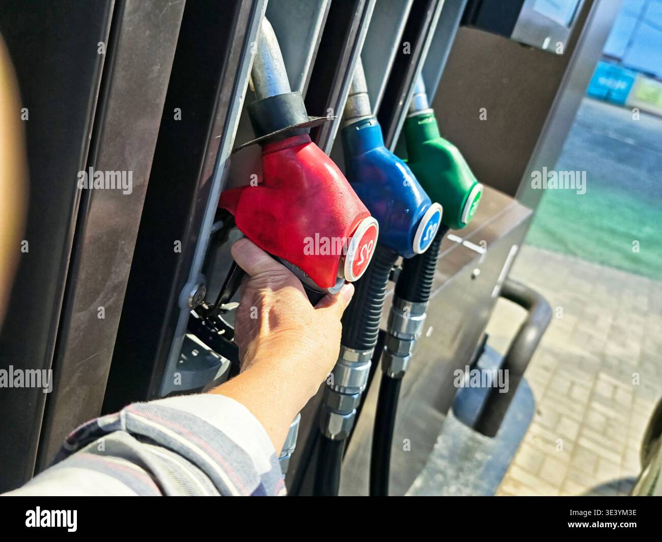 Eine Hand hält eine Kraftstoffdüse an einer Tankstelle, während das Fahrzeug vor der Weiterfahrt aufgefüllt wird. Der Himmel ist klar. Stockfoto