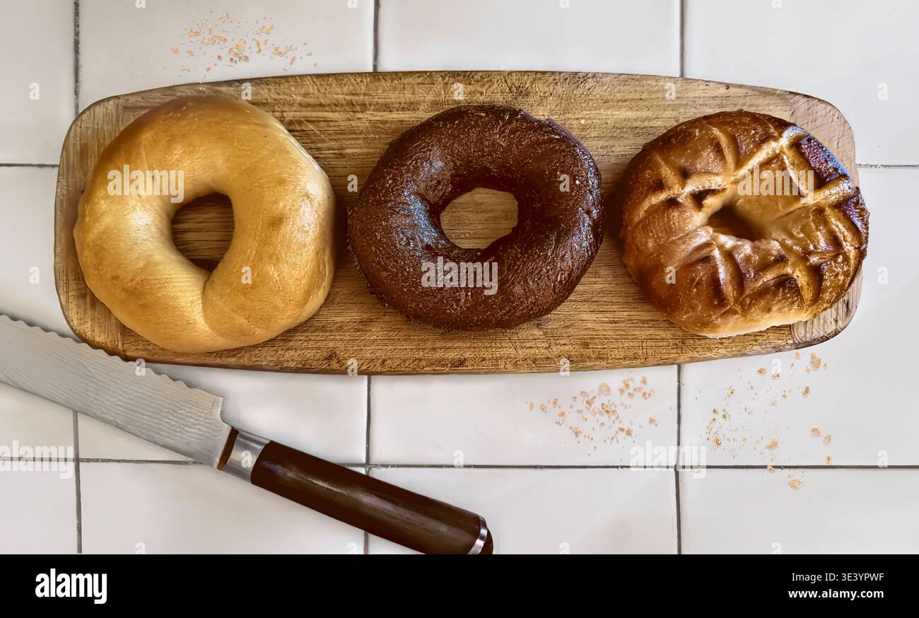 Frische Bagels auf hölzernem Schneidebrett und Fliesentheke. Stockfoto