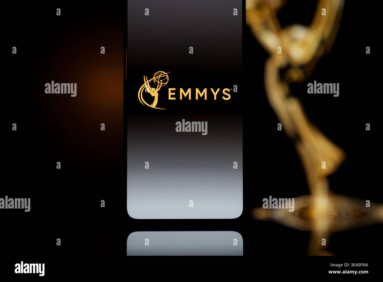 Emmys Logo auf einem Smartphone-Bildschirm mit einer verschwommenen Gold-Auszeichnung im Hintergrund, TV-Industrie-Auszeichnungen und Digital Streaming Co Stockfoto