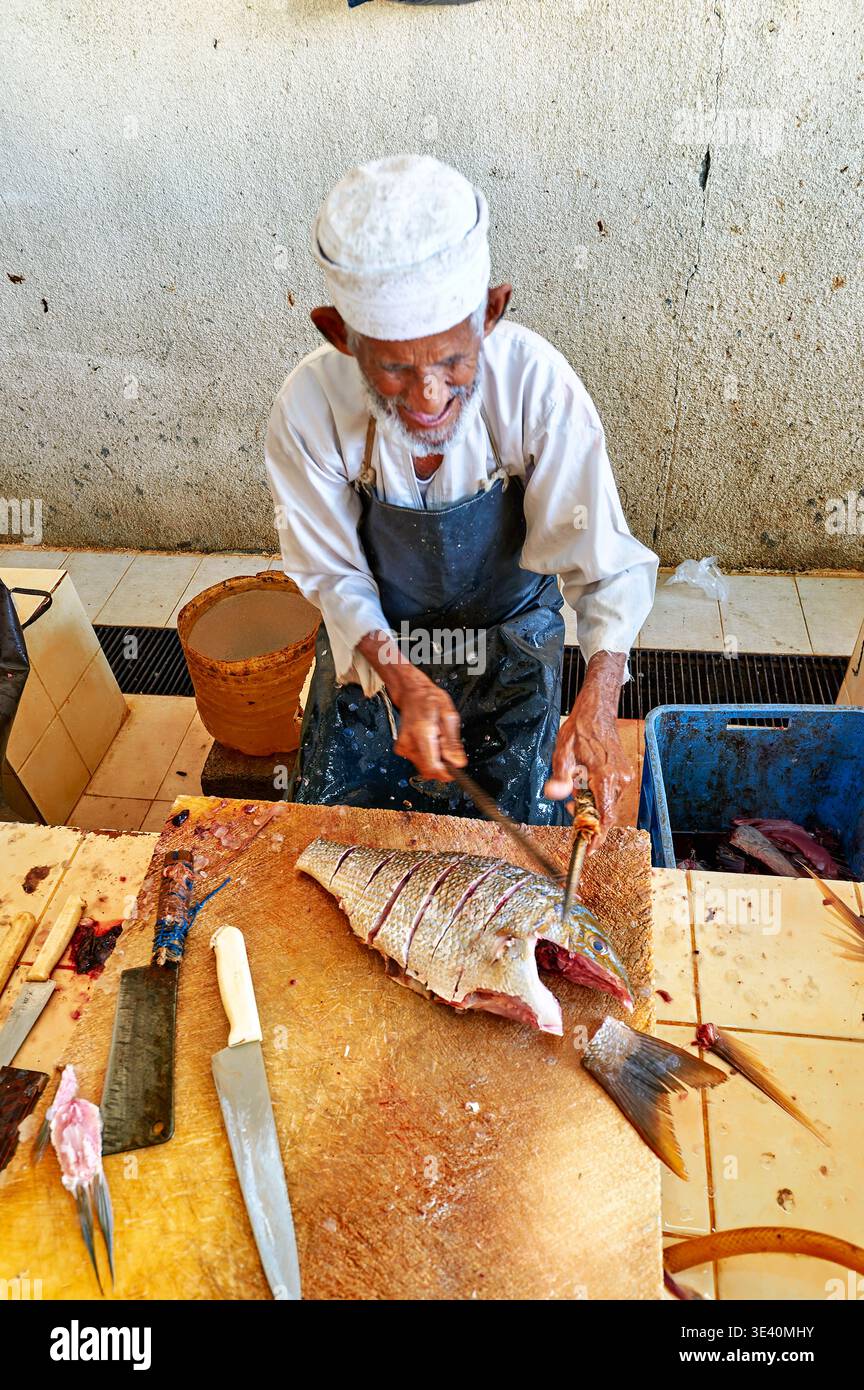 Ein Fischer schneidet Fisch auf dem Muscat Oman Fischmarkt. Es ist eine geschäftige Szene mit lokalen Anbietern und frischen Fängen des Tages. Stockfoto