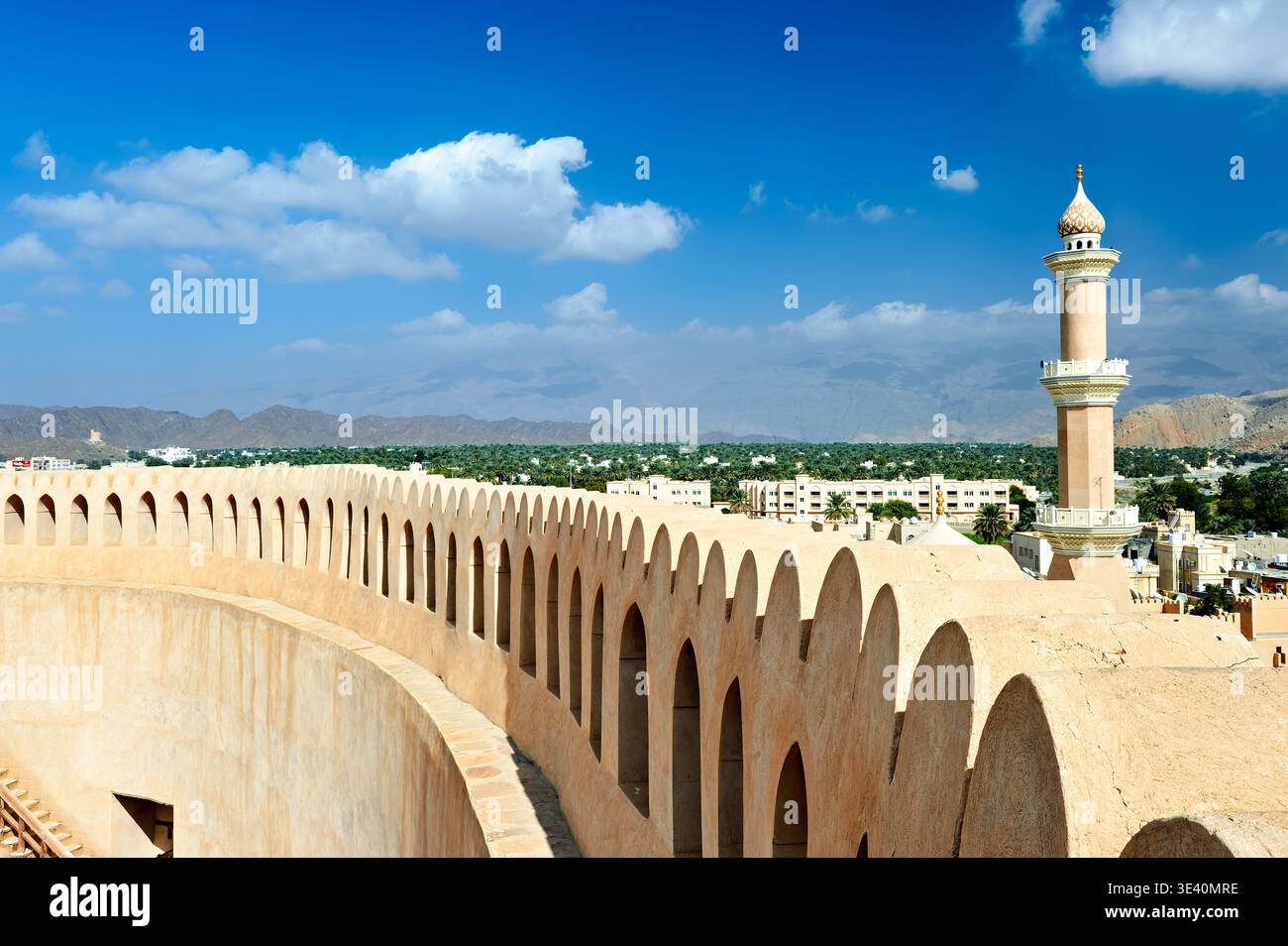 Nizwa Fort steht stark gegen den Himmel. Besucher erkunden die Stadtmauern und genießen dabei den Blick auf die Stadt und die umliegenden Berge. Stockfoto
