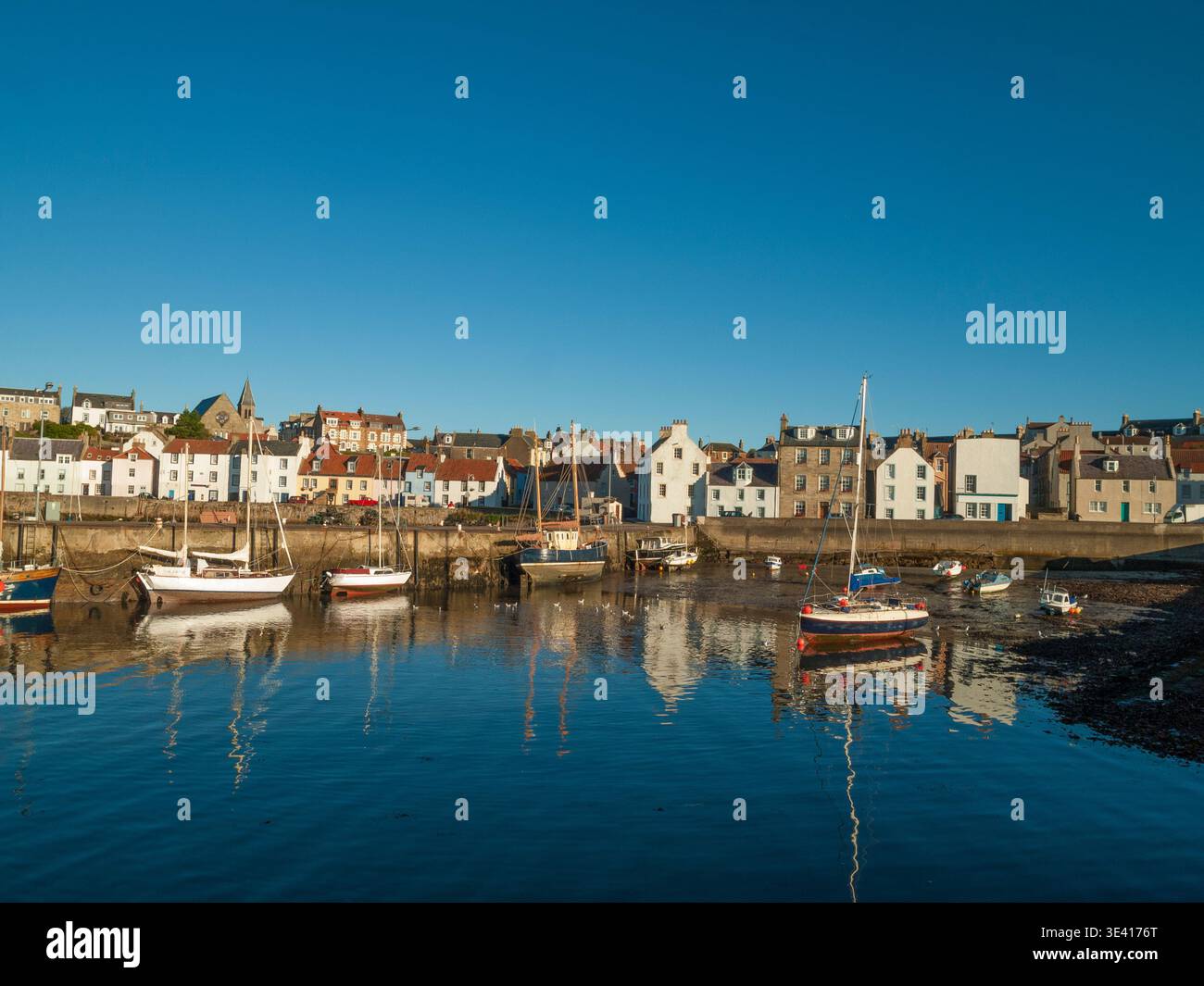 Bei Ebbe liegen farbenfrohe kleine Boote im Hafen von St Monans, deren Reflexionen sich im ruhigen Wasser neben Reihen traditioneller Küstenhäuser und spiegeln Stockfoto