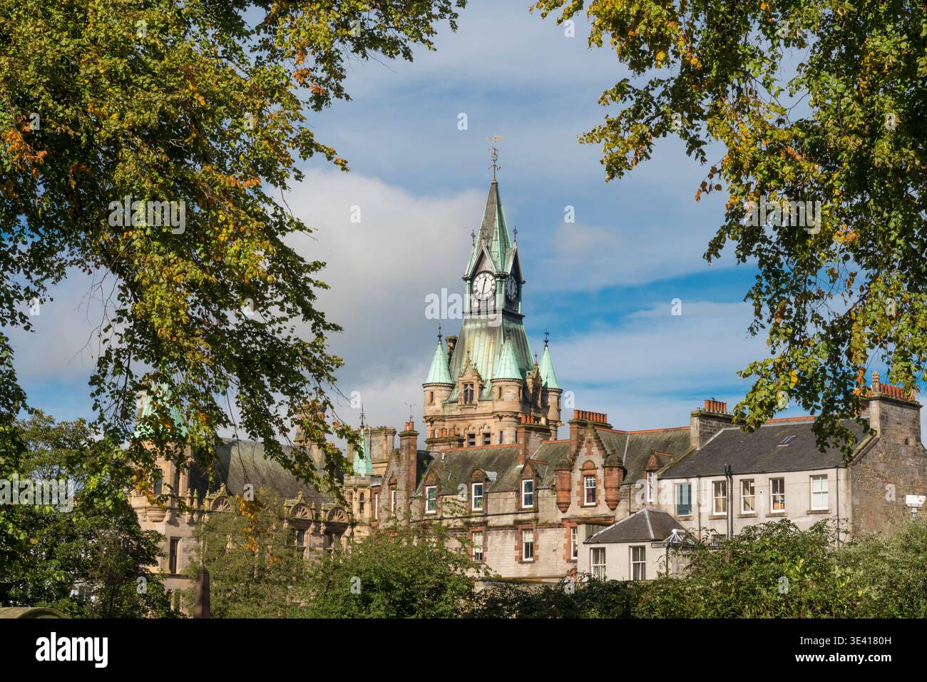 Der historische Uhrenturm Dunfermline City Chambers erhebt sich über steinigen Stadthäusern, eingerahmt von grünen Bäumen und blauem Himmel, die an den Stolz der Bürger und das Erbe erinnern Stockfoto
