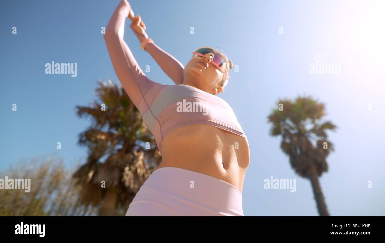 Frau in rosa Oberteil und weißen Shorts, die unter Palmen trainiert Stockfoto