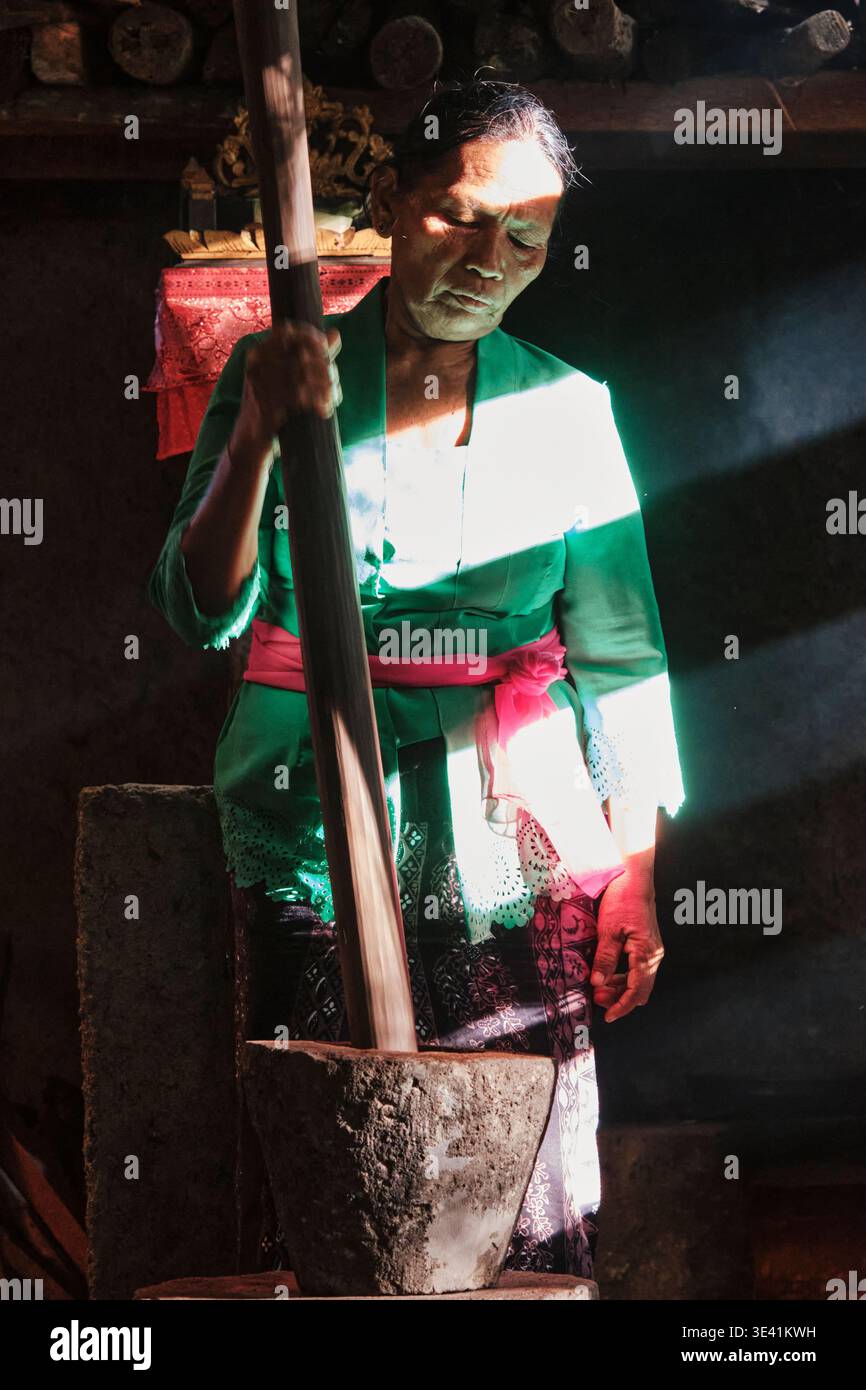 Eine balinesische Frau in Badung, Bali, mahlt Zutaten in einer traditionellen Küche in Bali. Das Sonnenlicht scheint durch das Fenster und erzeugt Muster. Stockfoto