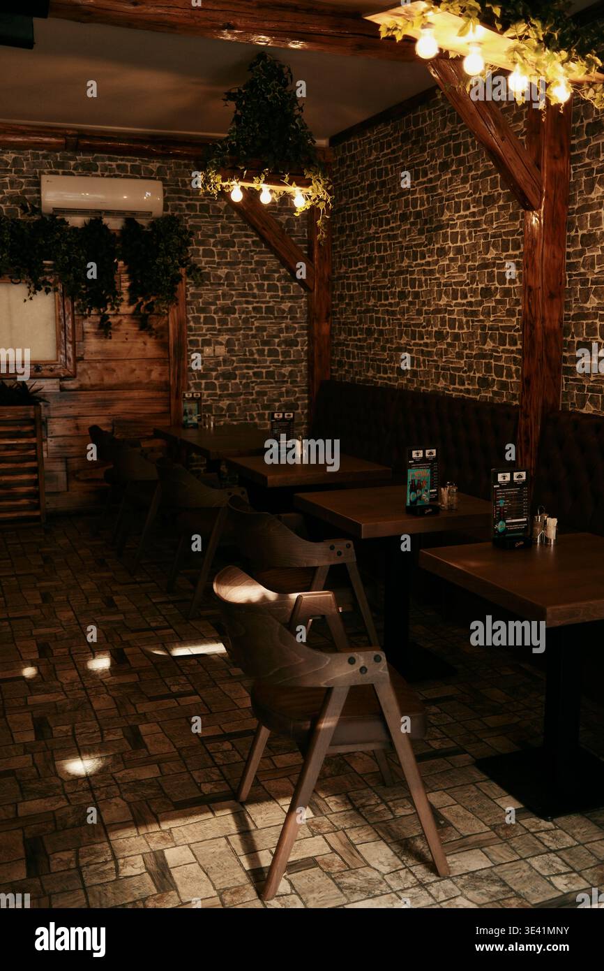 Gemütliches Innere des Restaurants mit Holztischen, Stühlen und warmem Licht schafft eine intime Atmosphäre. Sombor, Serbien - 13. März 2026. Stockfoto