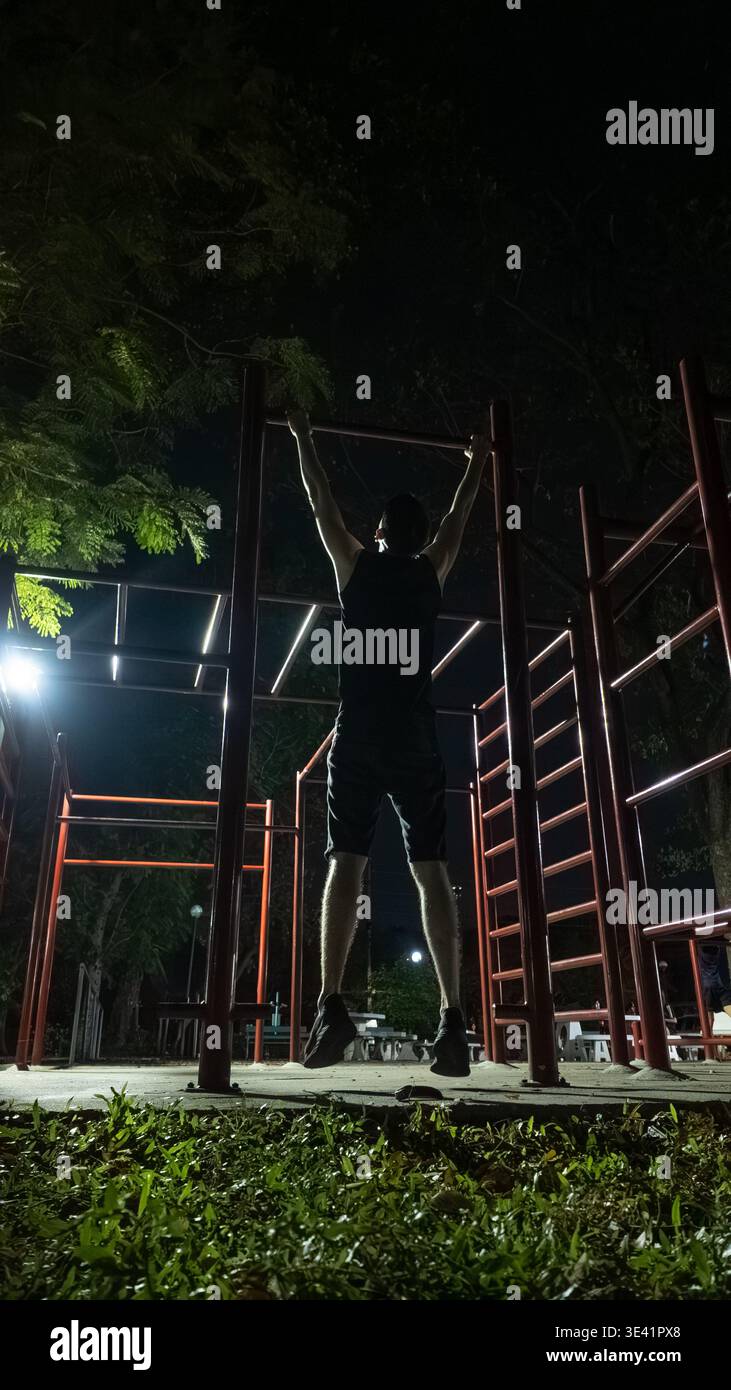 Ein Mann, der nachts an den Bars im Freien trainieren kann, ein männlicher Athlet, der im Park Calisthenics-Workout durchführt Stockfoto