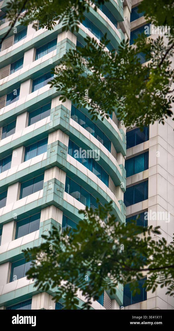 Modernes Hochhaus mit blauer und weißer Fassade, blau getönten Fenstern und Bäumen im Vordergrund. Stockfoto