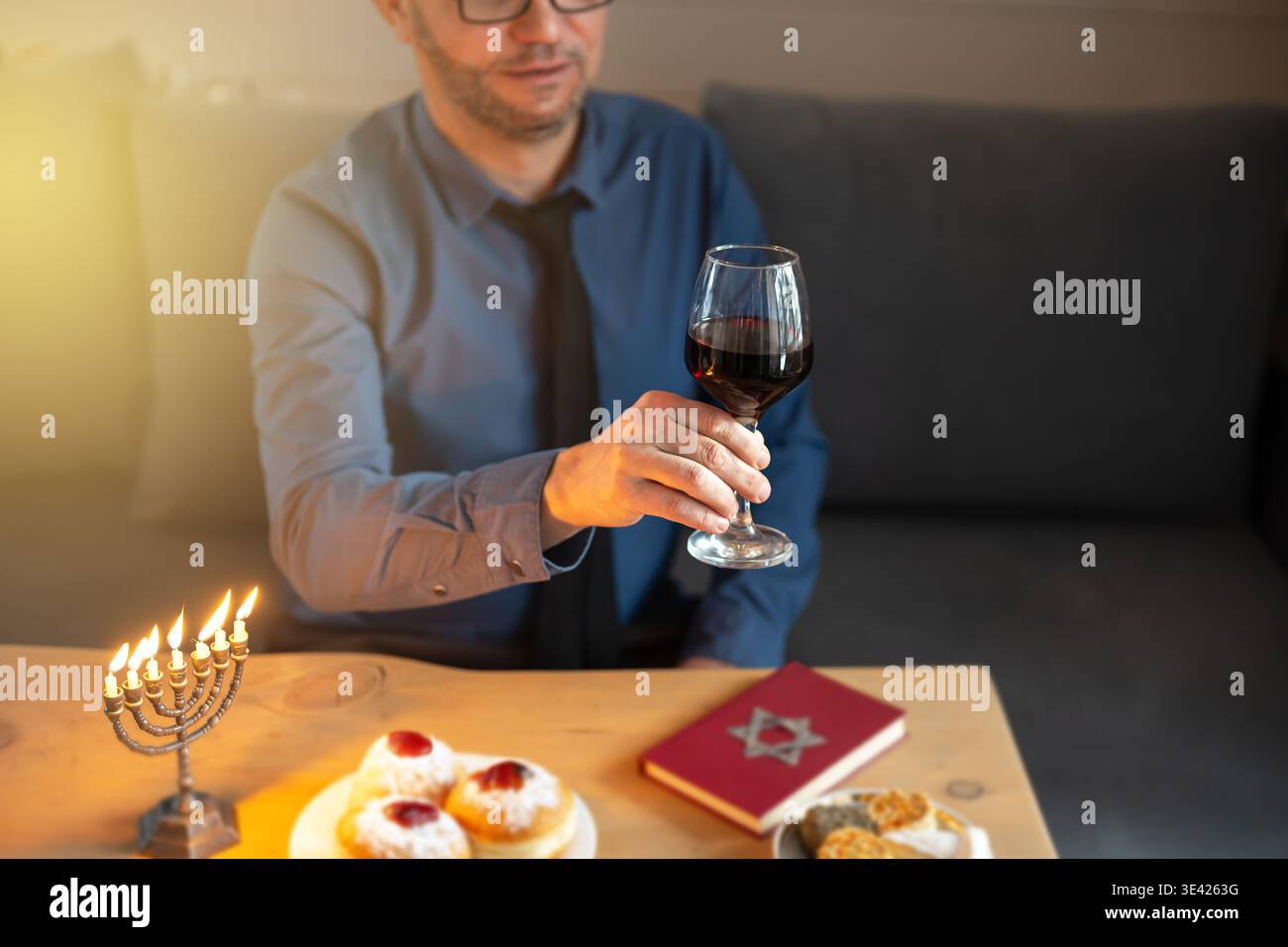 Jüdischer Mann feiert Hanukkah zu Hause, hebt ein Glas koscheren Rotweins auf, um seine Familie zu begrüßen. Traditioneller jüdischer religiöser Feiertag. Happy Hanukkah Concept Stockfoto
