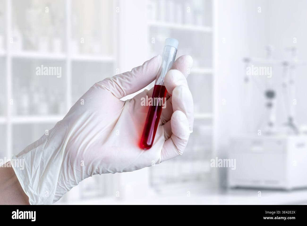 Nahaufnahme eines Handteströhrchens mit roter Flüssigkeit, Laboranalysekonzept auf hellem klinischem Hintergrund Stockfoto
