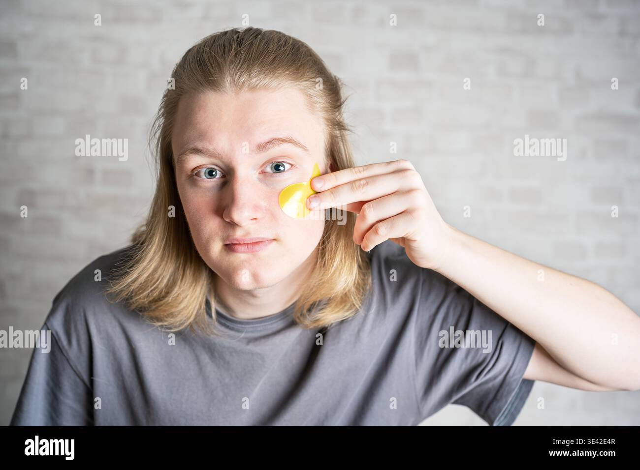 Junger gutaussehender blonder Mann, der gelbe Augenflecken aufträgt, Kopierraum. Beauty-Routine, mit feuchtigkeitsspendenden Gesichtspflecken. Stockfoto