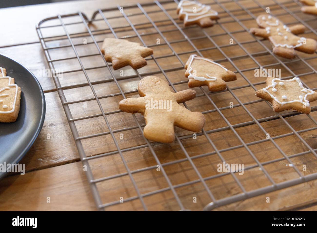 Lebkuchenmensch kühlt auf einem Gittergestell an einer Holzplatte mit weißer Glasur und dunkler Keramikplatte ab Stockfoto