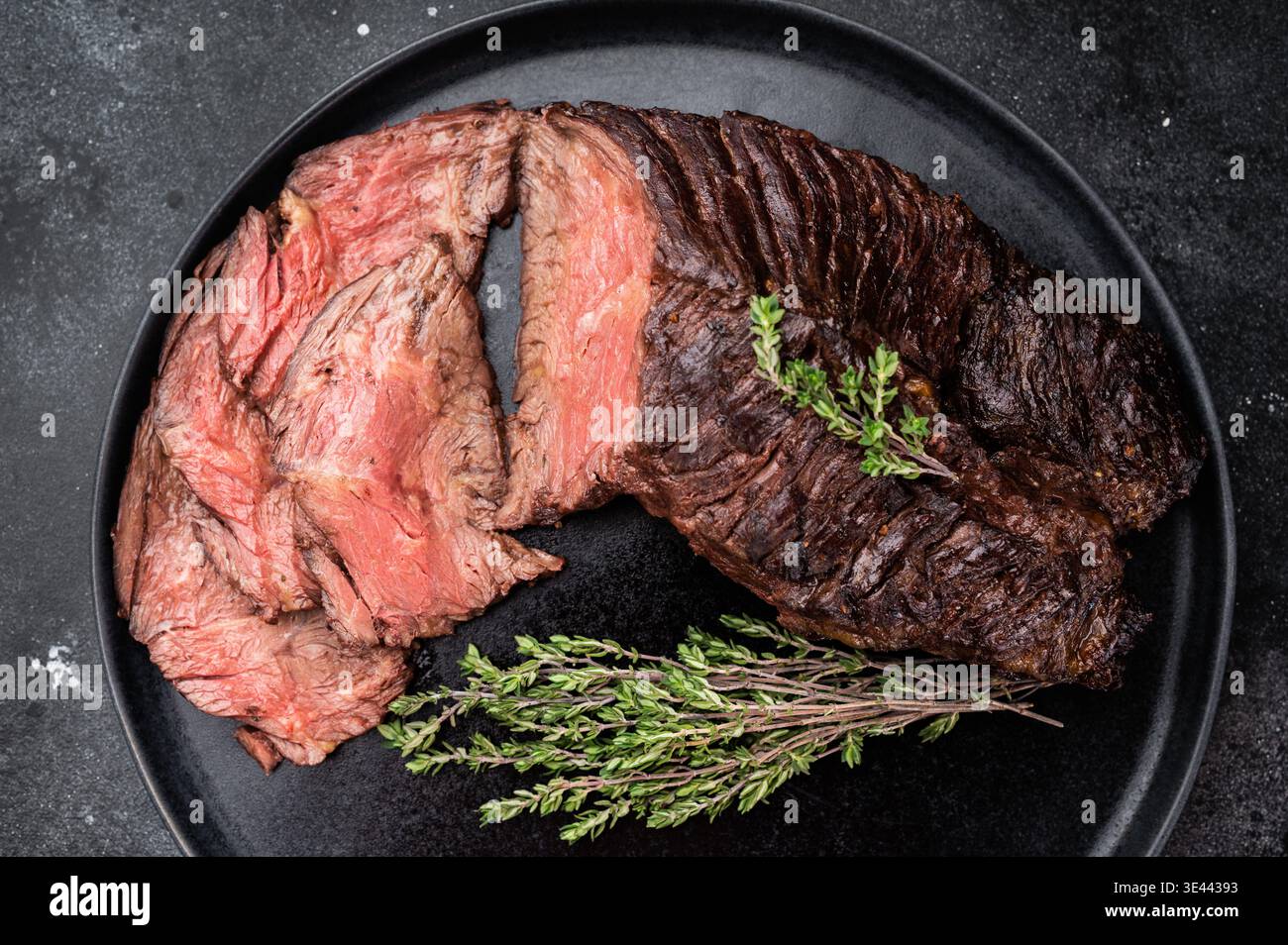 Geschnittenes gegrilltes Rindersteak oder Onlet Steak auf schwarzem Teller mit Thymian und Salz, dunkler Steinhintergrund mit Kopierraum Stockfoto