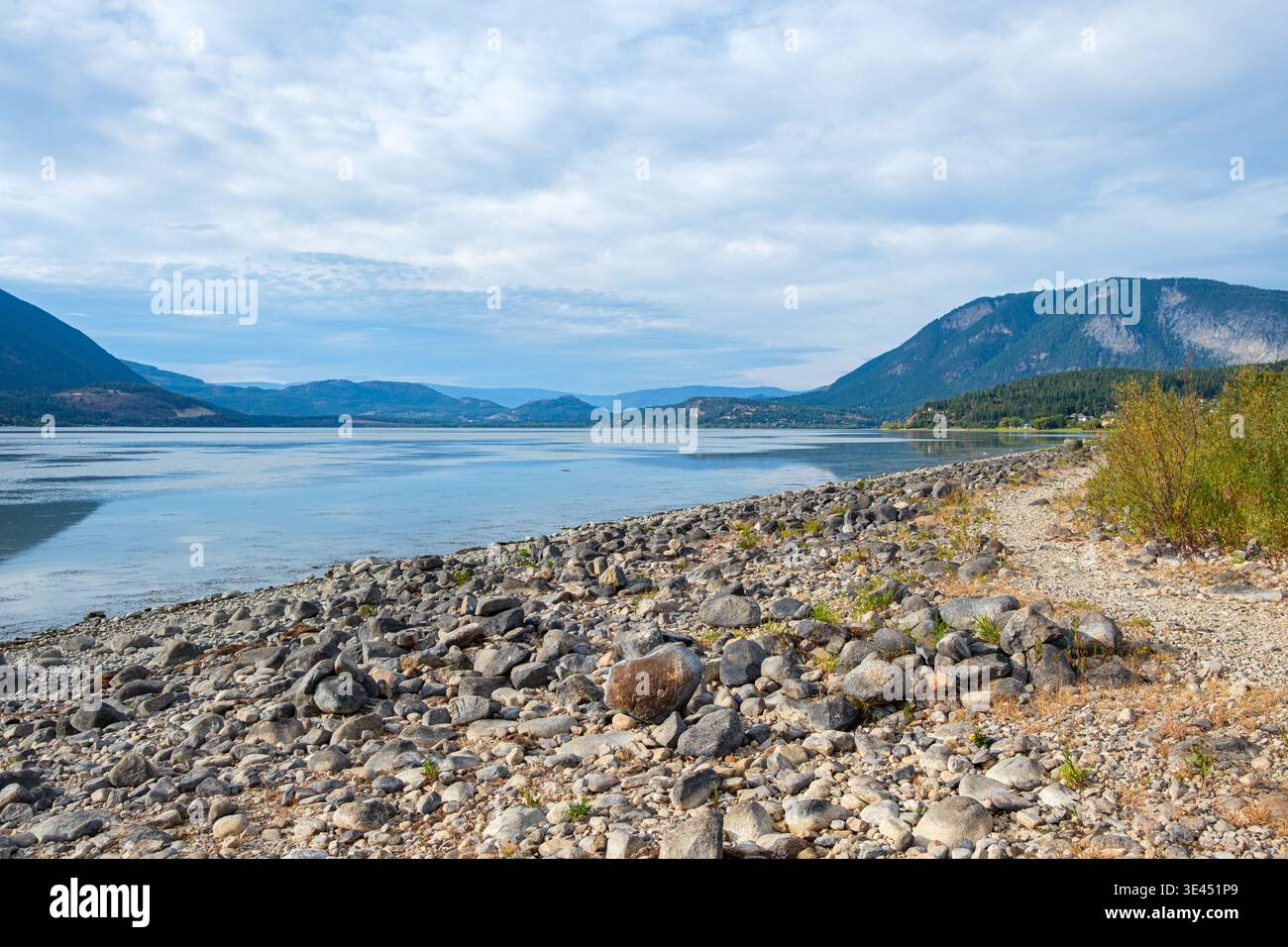 Vom steinigen Strand in Salmon Arm, BC, mit Blick nach Norden entlang des ruhigen Wassers des Shuswap Lake zu bewaldeten Hügeln und Bergen in der Ferne. Stockfoto