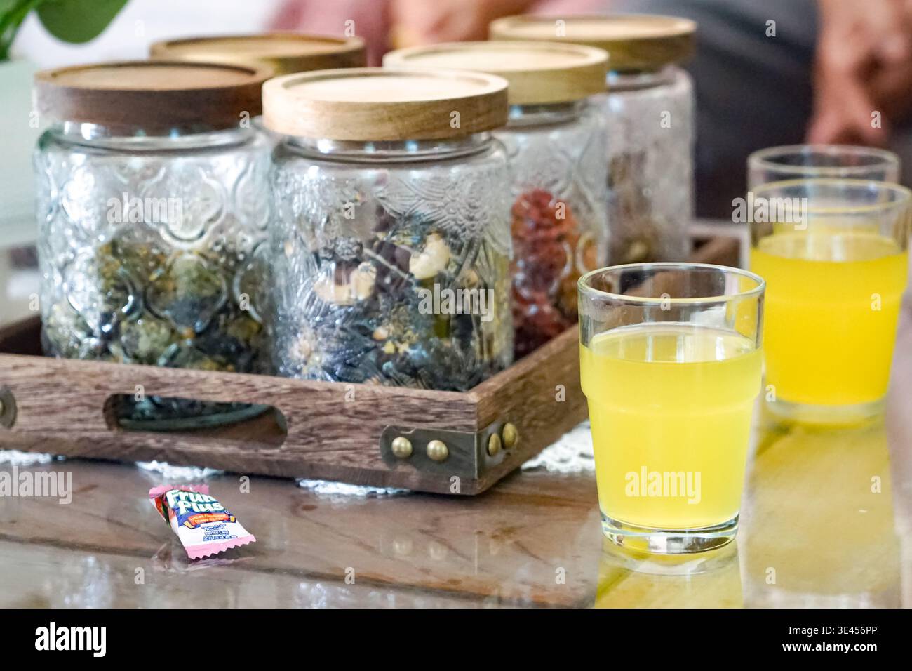 Dekorative Gläser mit Holzdeckeln und einem Glas gelben Saft auf einem Tablett neben einer Topfpflanze. Stockfoto