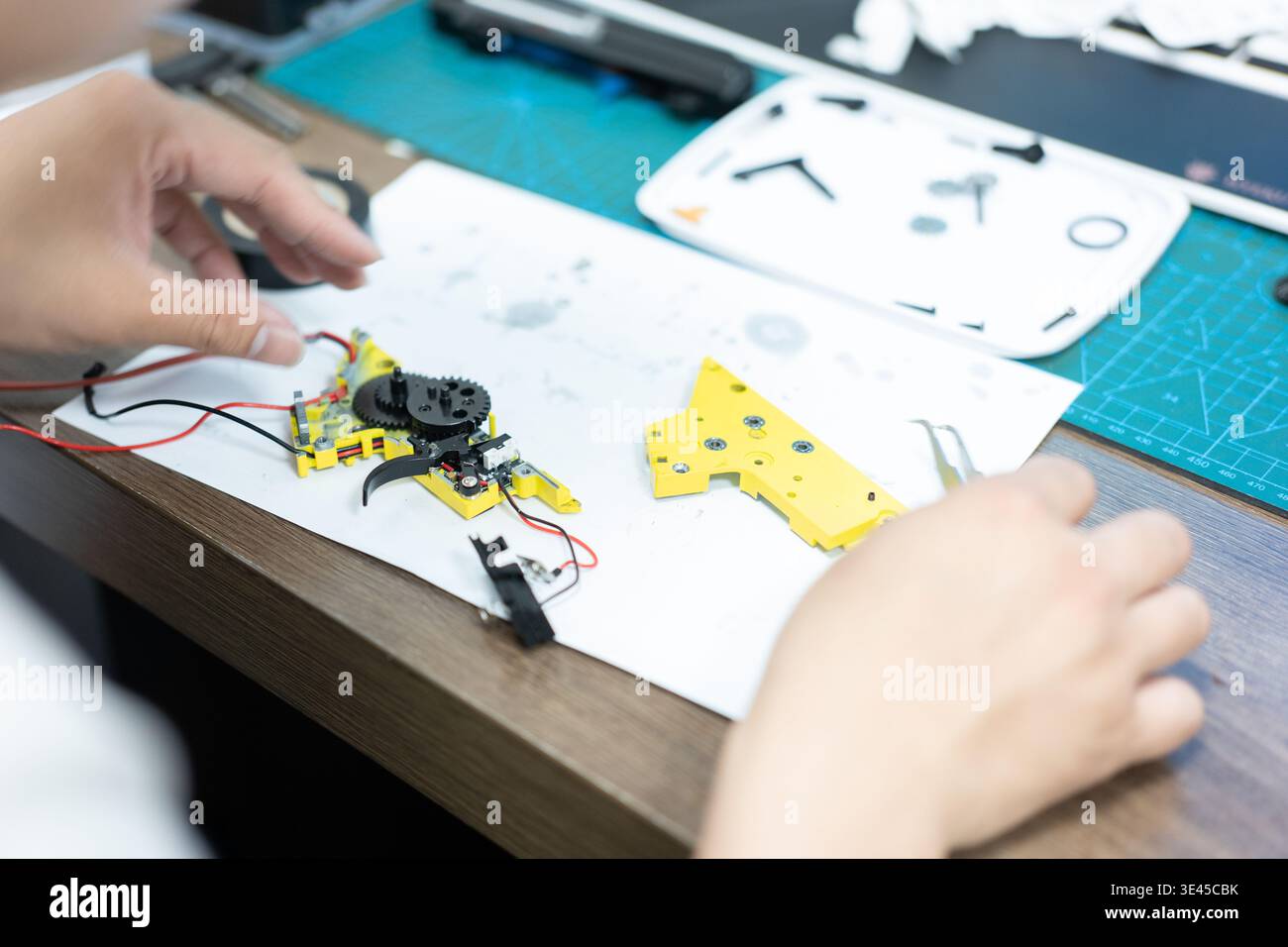 Hände, die gelbe mechanische Teile mit Verkabelung auf Werkbank in der Werkstatt montieren, Nahansicht Stockfoto