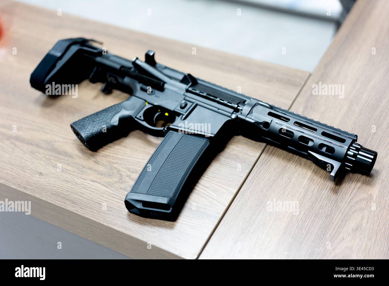 Schwarzes Gewehr im Stil AR-15 mit zusammenklappbarem Schaft auf Holztisch in moderner Inneneinrichtung Stockfoto
